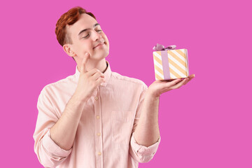 Thoughtful young redhead man with gift box on purple background