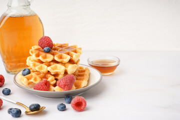Plate of tasty waffles with berries and maple syrup on white background