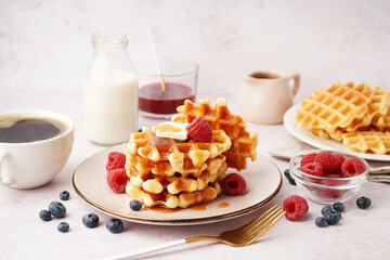 Tasty waffles with berries, maple syrup and cup of coffee on white background