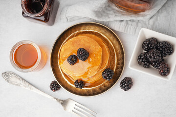 Plates of tasty pancakes with blackberries and maple syrup on white background