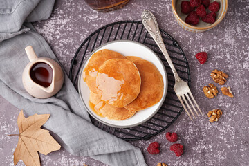 Plate of tasty pancakes with raspberries and maple syrup on grey background