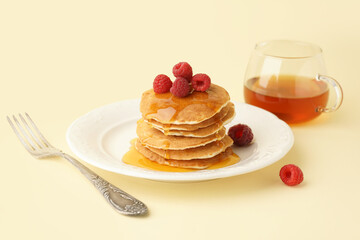 Plate of tasty pancakes with raspberries and maple syrup on yellow background