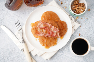 Tasty pancakes with bacon, maple syrup, nuts and cup of coffee on white background