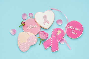 Pink cookies with ribbons, flowers and supportive words on blue background. Breast cancer awareness concept