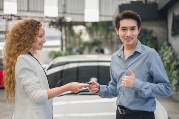 A beautiful female car sales employee gives the keys to the customer who has duly signed the...