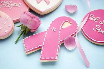 Pink cookie in shape of ribbon with rose flower on blue background, closeup. Breast cancer awareness concept - obrazy, fototapety, plakaty