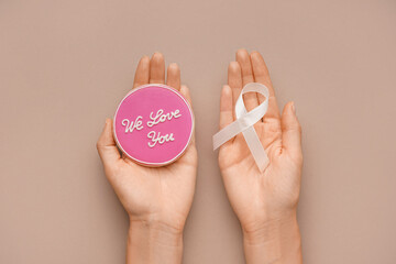 Female hands holding cookie with text WE LOVE YOU and ribbon on brown background. Breast cancer awareness concept