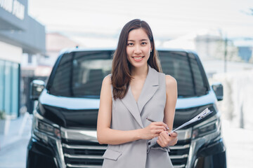 Professional female salesperson Asia at car dealership. Posing proudly at auto showroom, smiling to...