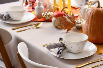 Elegant table setting with clean dishes, golden cutlery and pumpkins for Halloween party