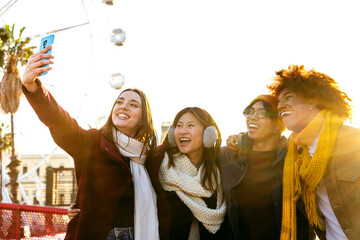 Happy multiracial smiling college friends taking selfie together in a sunny winter day in the city...