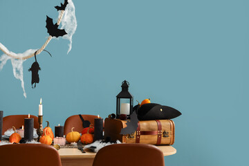 Festive table setting for Halloween party with burning candles, pumpkins and bats on blue background