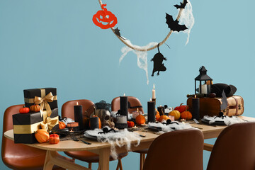 Festive table setting for Halloween party with burning candles, pumpkins and bats on blue background