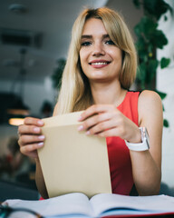 Cheerful young female employee opening envelope in cafe