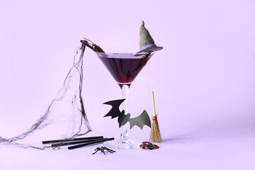 Glass of delicious cocktail for Halloween celebration on purple background