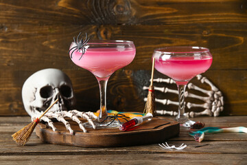 Glasses of delicious pink cocktail and skeleton hands for Halloween celebration on wooden background