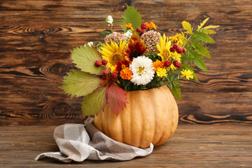 Beautiful autumn bouquet with leaves in pumpkin on wooden background
