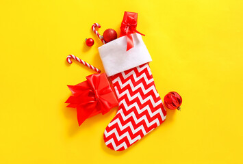 Fototapeta na wymiar Christmas sock with balls, candy canes and gift boxes on yellow background