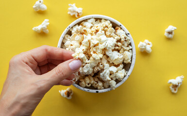A woman's hand takes popcorn from a cup.