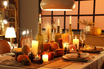Festive table setting with burning candles, pumpkins and greeting cards for Thanksgiving Day at evening