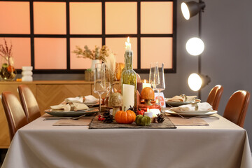 Beautiful table setting with burning candles, pumpkins and greeting cards for Thanksgiving dinner at evening