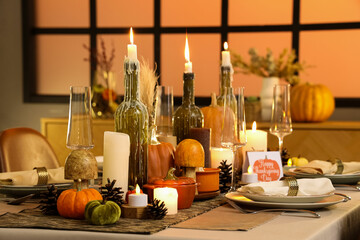 Beautiful table setting with burning candles, pumpkins and greeting cards for Thanksgiving dinner at evening