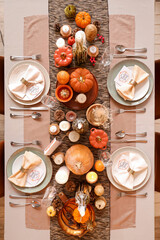 Beautiful table setting with burning candles, pumpkins and greeting cards for Thanksgiving dinner,...