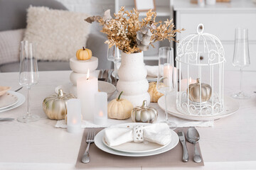 Elegant table serving with pumpkins and burning candles for Thanksgiving dinner in light room