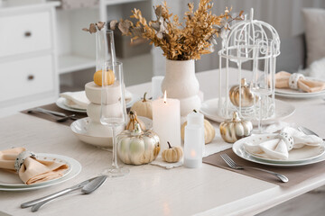 Elegant table serving with pumpkins and burning candles for Thanksgiving dinner in light room