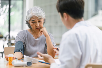 Obraz premium A young doctor using digital tonometer check blood pressure for senior woman. A doctor is holding a senior woman's hand.