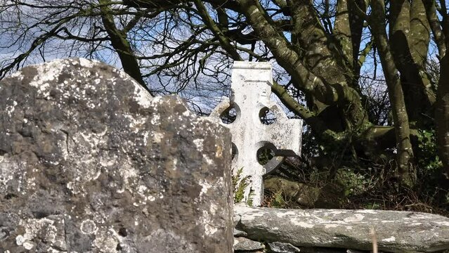 Old Irish Famine graveyard Celtic cross behind ancient headstone in spring