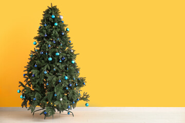 Christmas tree with blue baubles near yellow wall