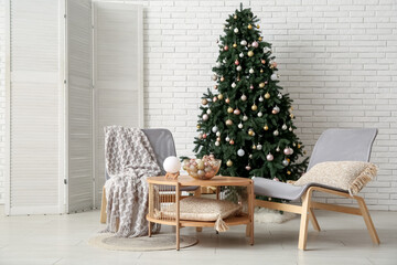 Interior of festive living room with Christmas tree, grey armchairs and coffee table