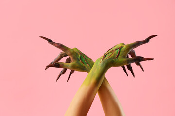 Hands of witch with claws on pink background. Halloween celebration