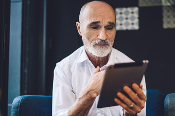 Grey haired stressed male browsing tablet