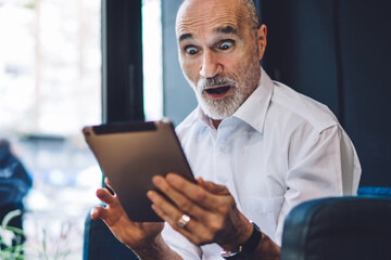 Elderly amazed man browsing tablet