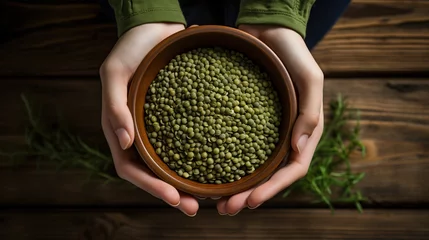 Tafelkleed Female hands holding a bowl of green lentils on a wooden table © PNG