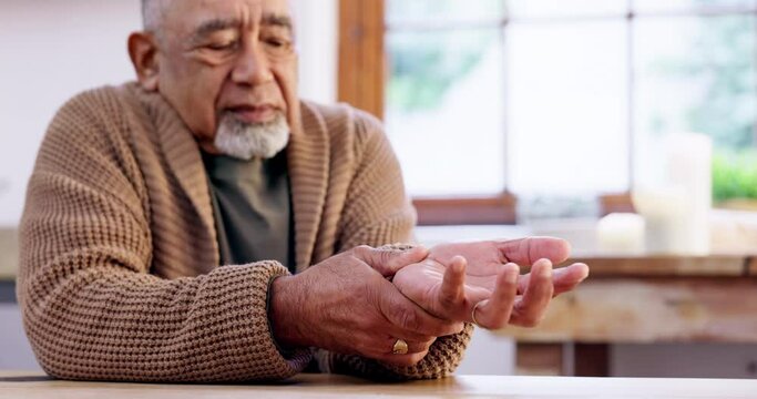 Hand, pain and senior man with arthritis, stress or unhappy with joint inflammation in a kitchen. Wrist, injury and elderly male with anxiety, discomfort or finger massage for muscle tension at home