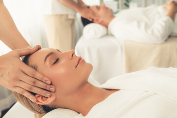 Fototapeta na wymiar Caucasian couple enjoying relaxing anti-stress head massage and pampering facial beauty skin recreation leisure in dayspa modern light ambient at luxury resort or hotel spa salon. Quiescent