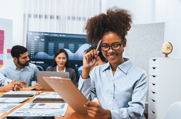 Happy young african businesswoman wearing glasses portrait with group of office worker on meeting with screen display business dashboard in background. Confident office lady at team meeting. Concord