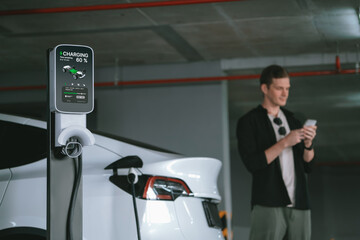 Young man travel with EV electric car to shopping center parking lot charging in downtown city...