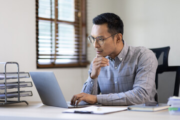 Fototapeta premium Portrait of Stylish Asian Businessman Works on Laptop, Does Data Analysis and Creative Designer, Looks at Camera and Smiles. Digital Entrepreneur Works on e-Commerce Startup Project