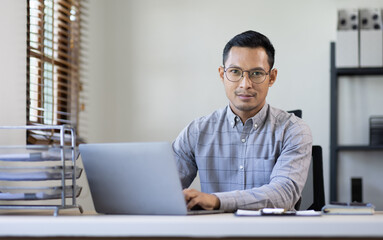 Obraz premium Portrait of Stylish Asian Businessman Works on Laptop, Does Data Analysis and Creative Designer, Looks at Camera and Smiles. Digital Entrepreneur Works on e-Commerce Startup Project