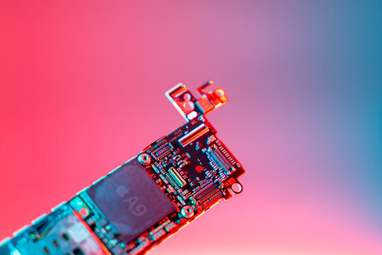 Kyiv, Ukraine - August 25, 2023: iPhone SE motherboard with Apple A9 processor, close-up on a rich color background. Gold company logo on the phone board