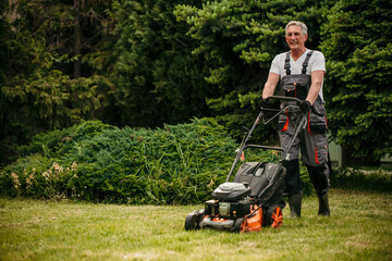 Senior man in work attire diligently mowing his backyard lawn on a sunny day