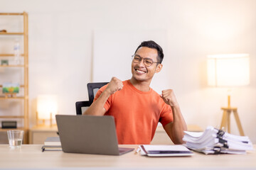 Excited Asian man sit at desk feel euphoric win online lottery, happy asian man overjoyed get mail at laptop being promoted at work, biracial man good news at computer - Powered by Adobe
