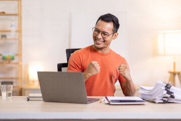 Excited Asian man sit at desk feel euphoric win online lottery, happy asian man overjoyed get mail at laptop being promoted at work, biracial man good news at computer