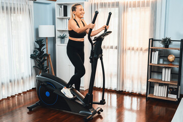 Fototapeta na wymiar Active senior woman running on elliptical running machine at home portrait in full body shot as fitness healthy lifestyle and body care after retirement for pensioner. Clout