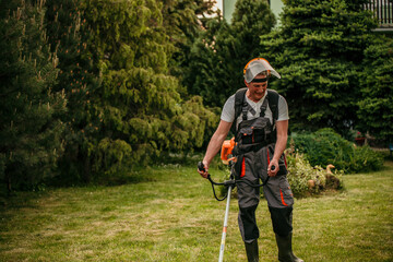 A mature man in a protective work suit showcasing his gardening prowess while operating a grass trimmer in his scenic outdoor space