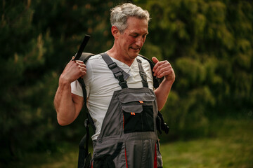 Senior gentleman taking a break from lawn maintenance, peeling off his work coveralls post-grass...