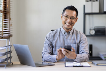 Fototapeta na wymiar Portrait of a cheerful man using smart phone at home office. freelance asian man entrepreneur and working from home research, planning and info 